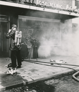 860045 Afbeelding van twee brandweerlieden die een kelderbrand bij schoenenzaak Neoform (St. Jacobsstraat 55) in Wijk C ...